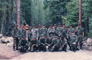 Group of soldiers in camouflage posing in a forest clearing.