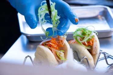 Chef wearing blue gloves prepares steamed buns with vegetables.