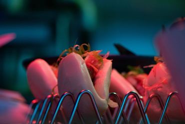 Close-up of bao buns on a metal rack under colorful lighting.