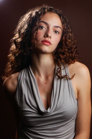 Curly-haired woman in gray sleeveless top.