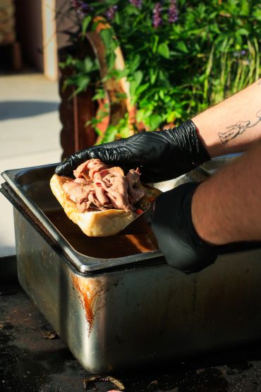 Person preparing a sandwich with meat.