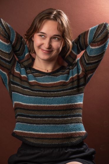 Smiling woman in a striped sweater with hands behind her head.
