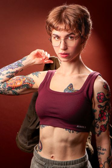 Young woman with glasses and tattoos poses confidently.