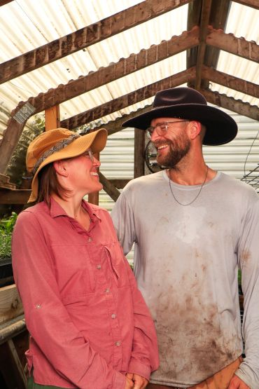 Happy couple in hats smiling inside a greenhouse.