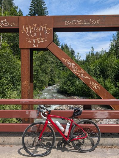 A gravel bike leaned against a metal bridge that spans across a small creek.