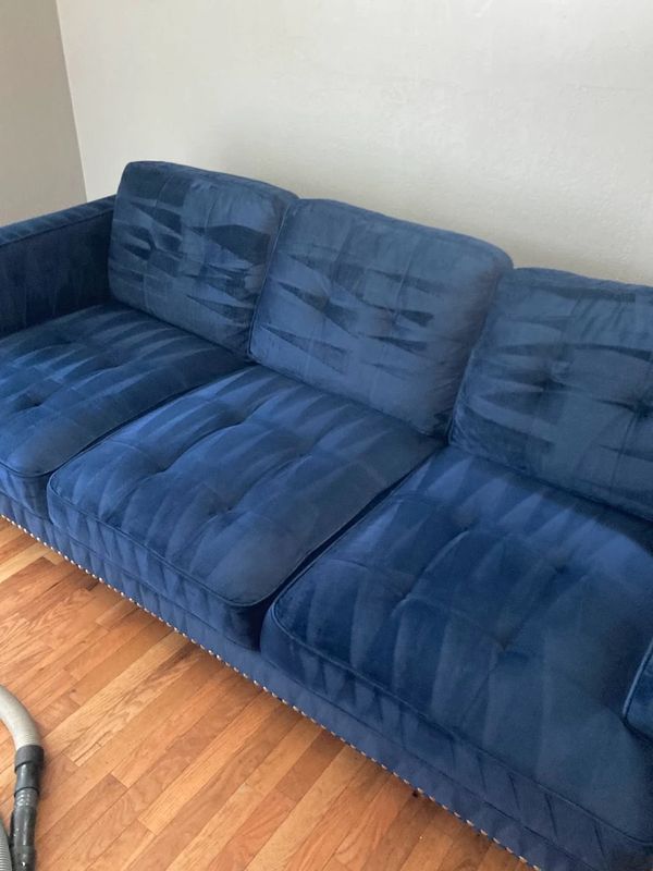 Blue velvet couch with tufted cushions on hardwood floor.