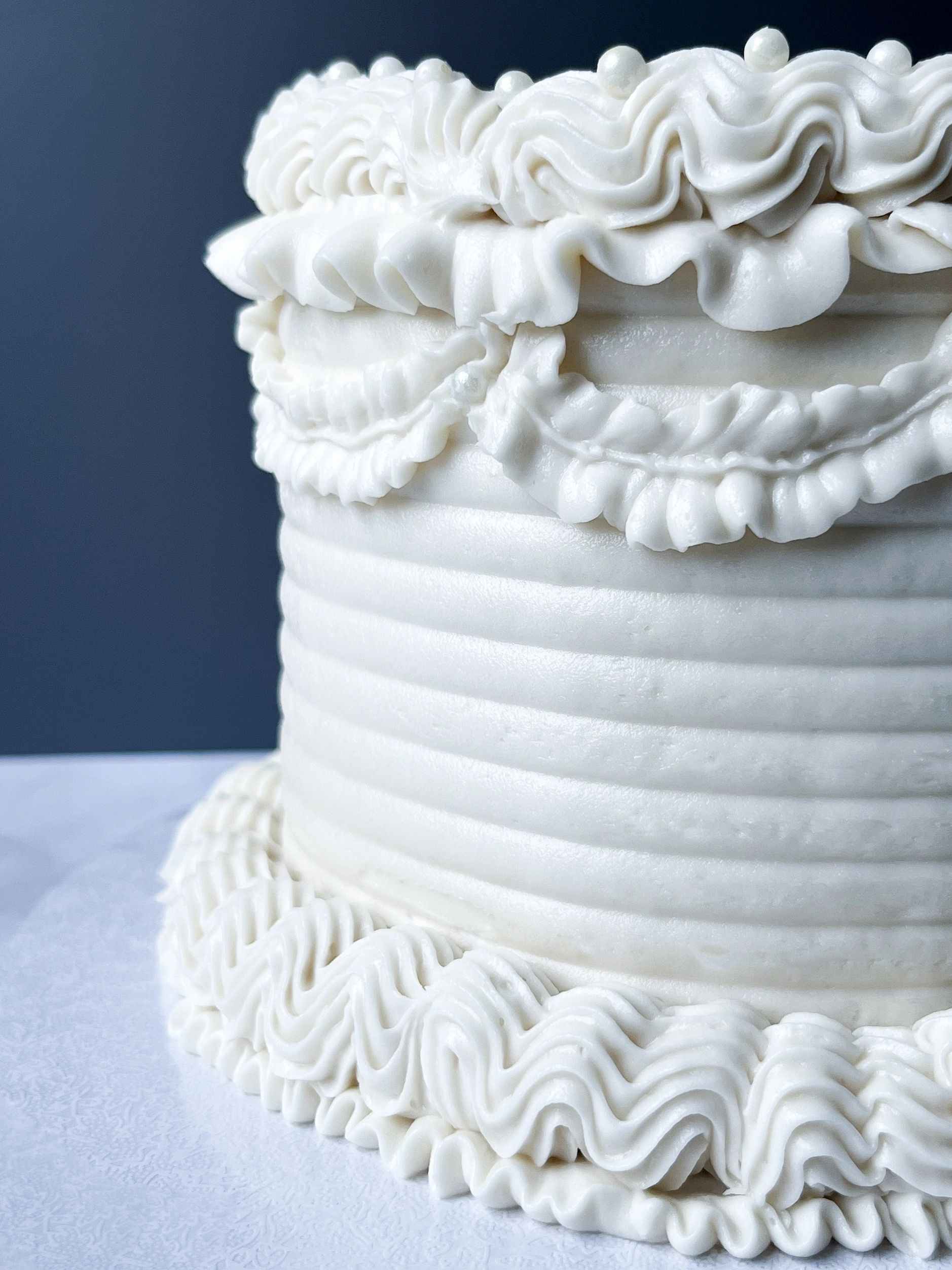 A white vintage piped cake in front of a dark background