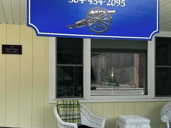 Front porch of Cannon Hill Inn with wicker furniture and a blue sign.