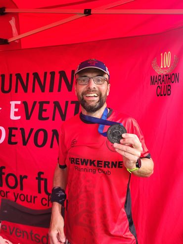 Runner proudly shows marathon medal under a red event tent.