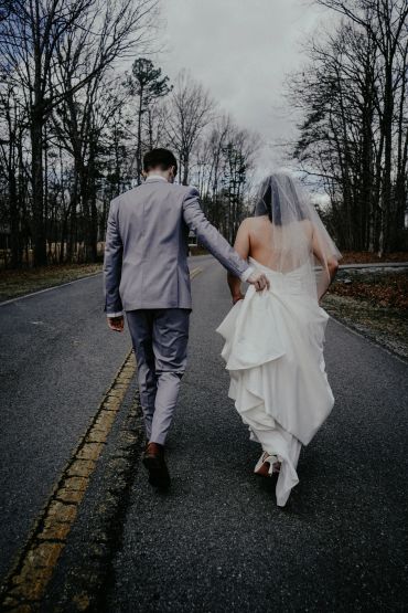 Bride and groom walking hand in hand down a deserted road.