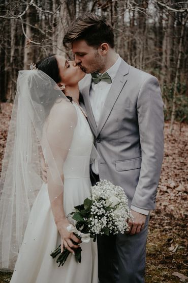 Bride and groom share a kiss in a forest setting on their wedding day.