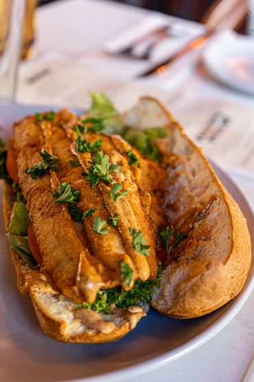 A fish sandwich garnished with fresh herbs on a white plate.