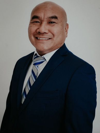 Smiling man in a blue suit and striped tie against a plain background.