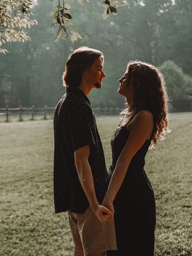 A couple holding hands, facing each other in a sunlit park.