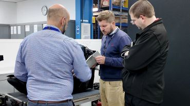 Three men examining a mechanical part in a workshop.