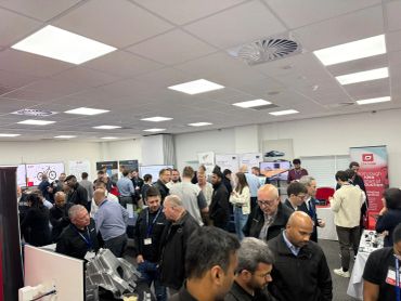 A busy indoor event with many people networking and exploring exhibits.