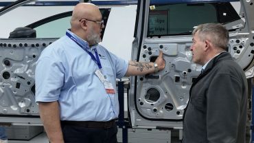 Two men discussing the inner workings of a car door at a trade show.