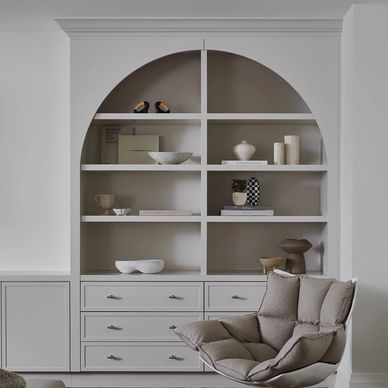 Minimalist shelf with decorative items beside a modern cushioned chair.