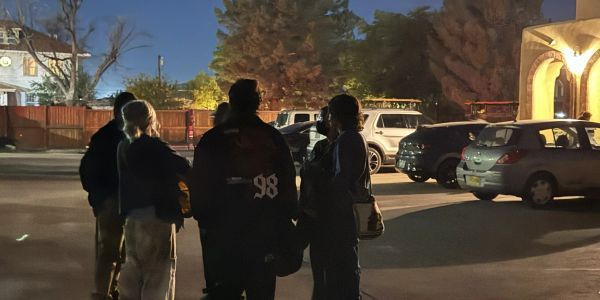 Group of people talking in a dimly lit parking lot at night.