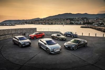 A lineup of six luxury cars parked near a waterfront at sunset.