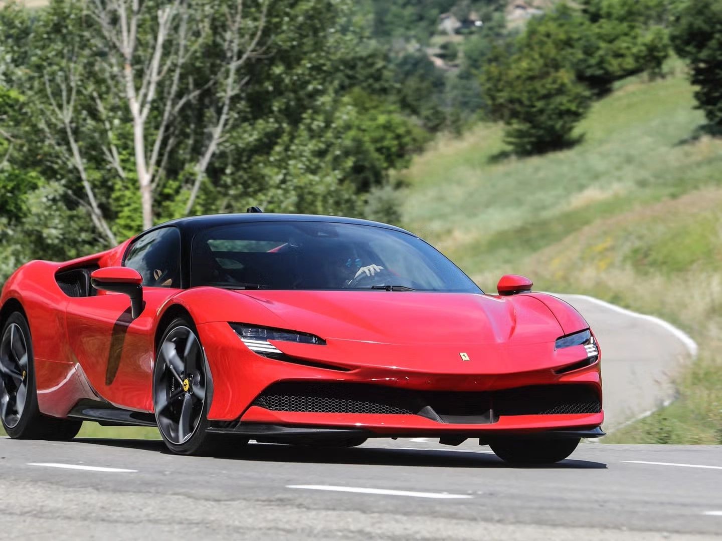 Red Ferrari sports car driving on a winding road surrounded by greenery.