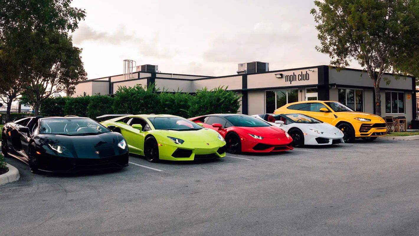 A lineup of colorful Lamborghini sports cars and an SUV parked outside mph club.
