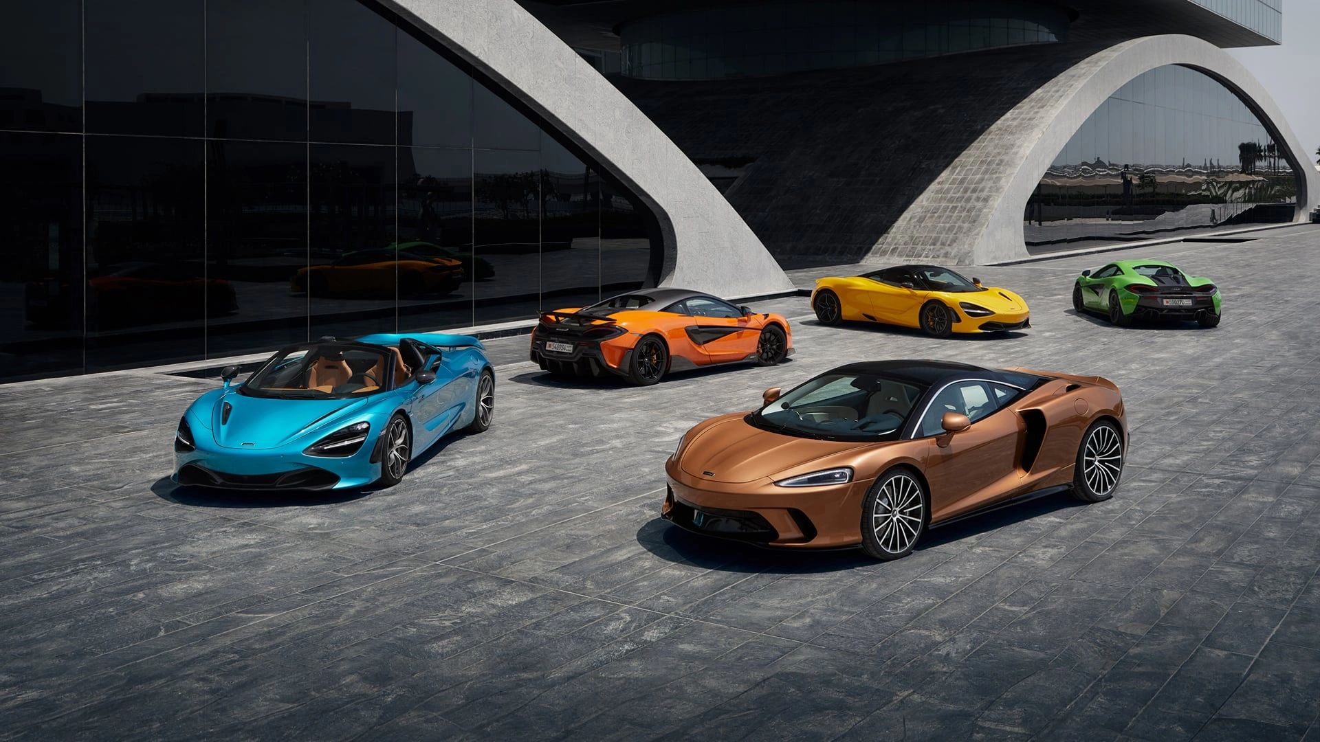 A lineup of colorful McLaren sports cars parked outside a modern building.