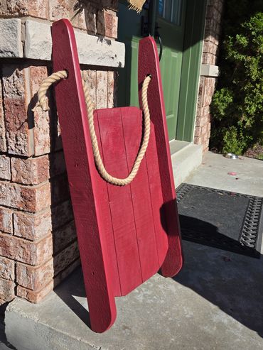 Red wooden sled leaning against a brick wall outside a house.