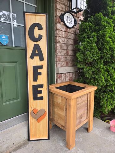 Wooden cafe sign leaning against a green door with a planter nearby.