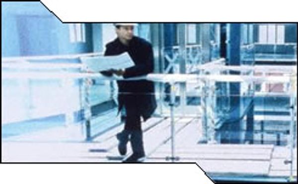 A blurred, blue-tinted image shows a person in a white hard hat holding papers, walking