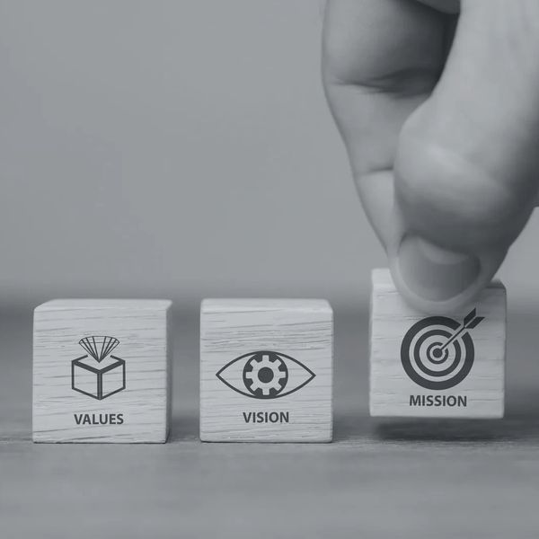 Hand placing a block labeled 'Mission' next to 'Values' and 'Vision' blocks.