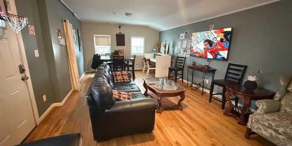 Cozy living room with leather sofas, wooden floor, and a TV on the wall.