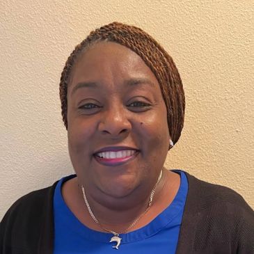 Smiling woman with braided hair wearing a blue top and black cardigan.