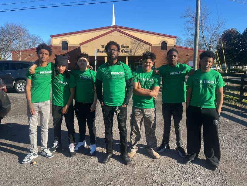 Seven young men wearing green 'Pierces' shirts standing outdoors in front of a building.