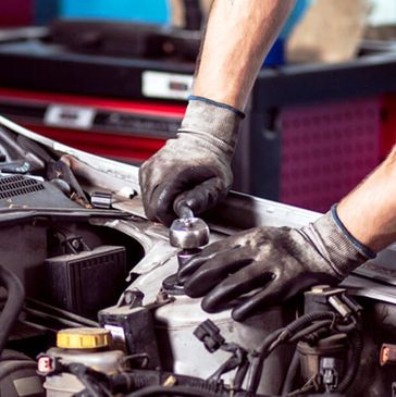 Mechanic wearing gloves repairing a car engine using a wrench.