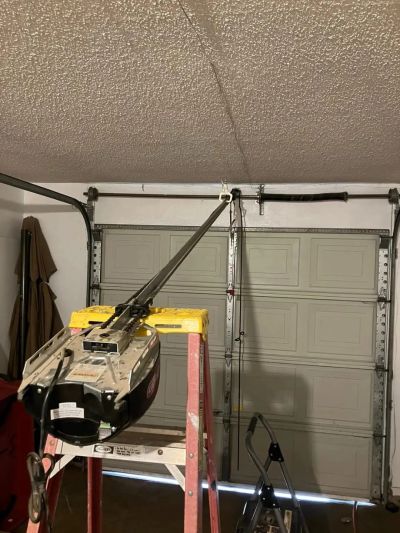 Garage door opener motor on a ladder in a garage.