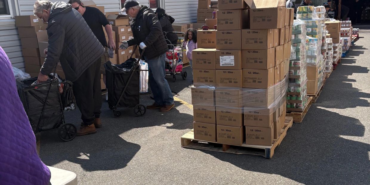 People gathering food supplies at an outdoor distribution site.