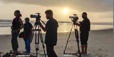 Filmmakers setting up cameras on a beach at sunset.