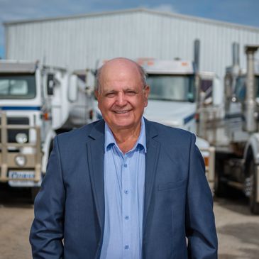 Smiling man in suit standing in front of trucks.