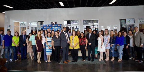 A large group of diverse professionals posing indoors with a PNC banner.