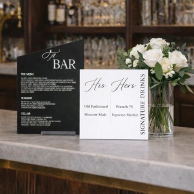 Two elegant bar menus and a vase with white flowers on a marble countertop.