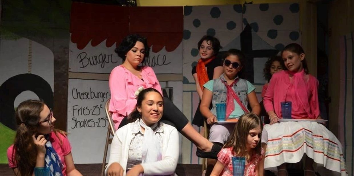 A group of girls in colorful outfits performing in a stage play.
