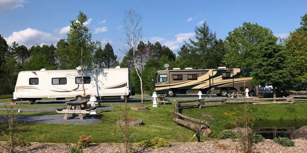 Two RVs parked in a green campground with picnic tables and trees.
