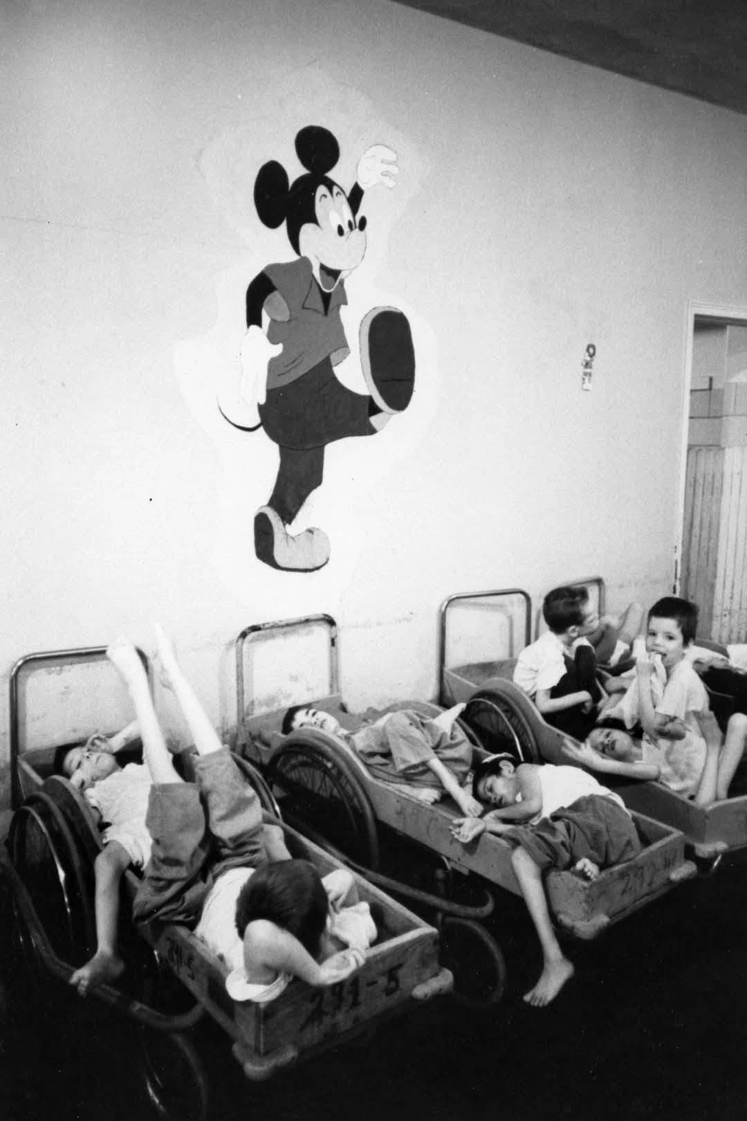 Children resting in wheelchairs under a Mickey Mouse wall painting.