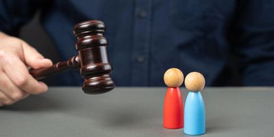 Judge's gavel poised above red and blue wooden figurines symbolizing judgment.