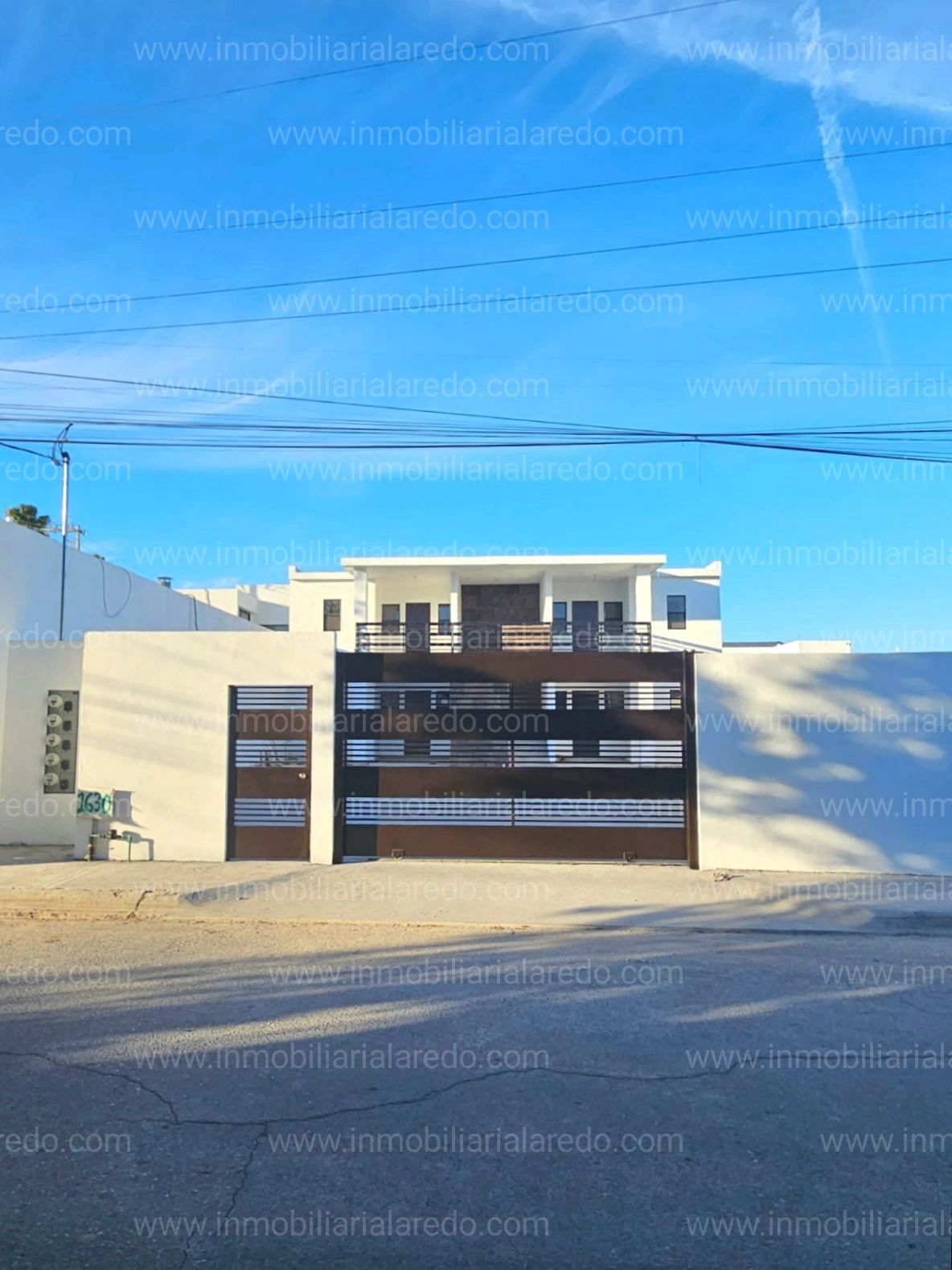 Fachada de casa moderna con portón metálico y muro blanco.