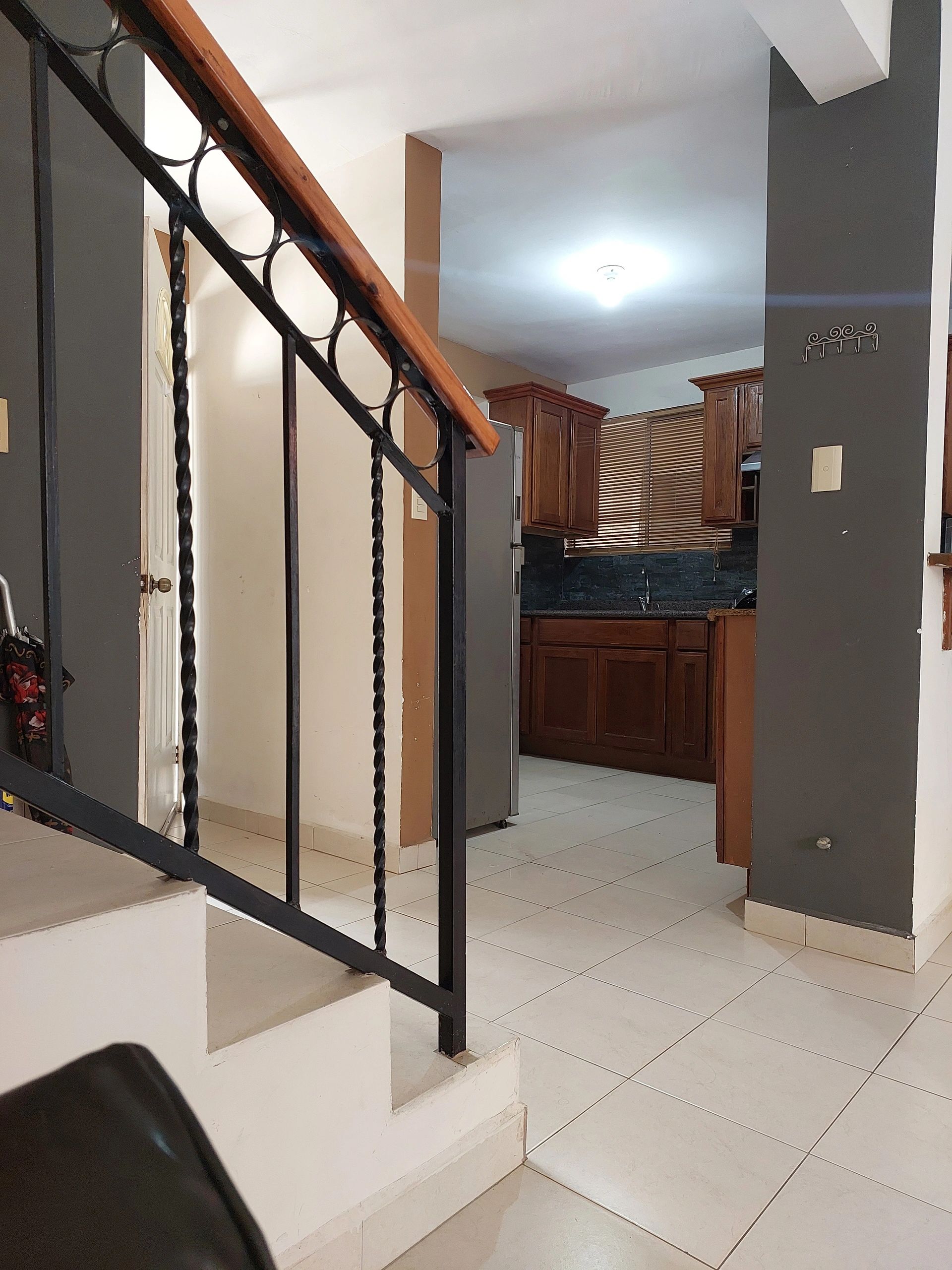 Interior view of a kitchen with wooden cabinets and a staircase with black railing.