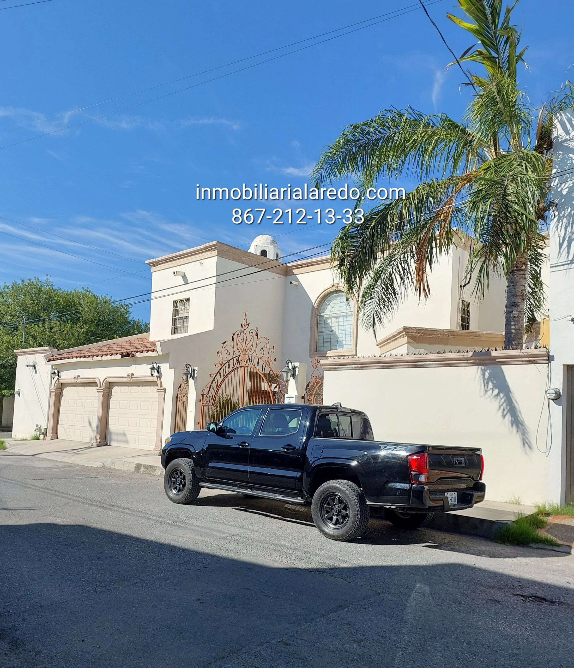Black pickup truck parked in front of a white house with palm trees under a clear blue sky.