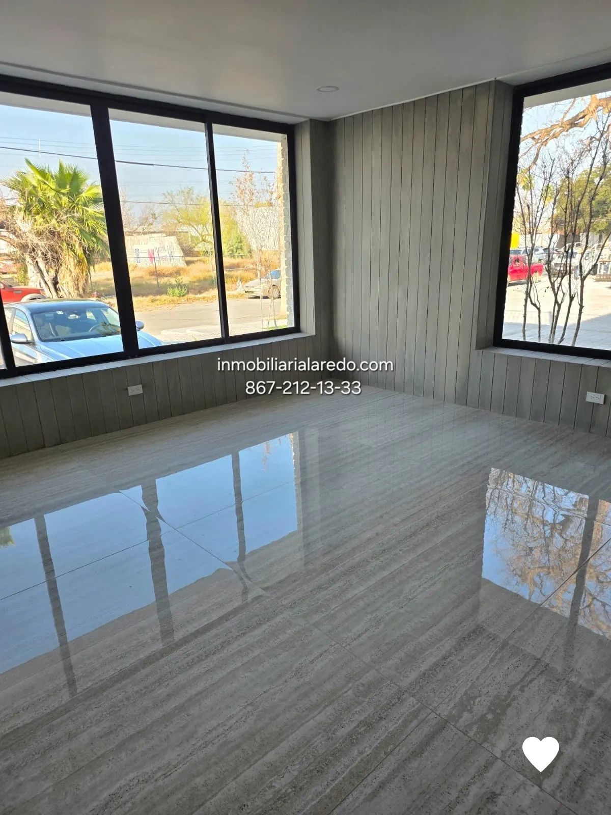 Bright empty room with large windows and reflective floor tiles.