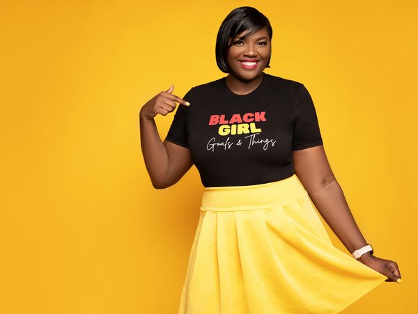 African American woman with a black shirt and yellow skirt smiling.